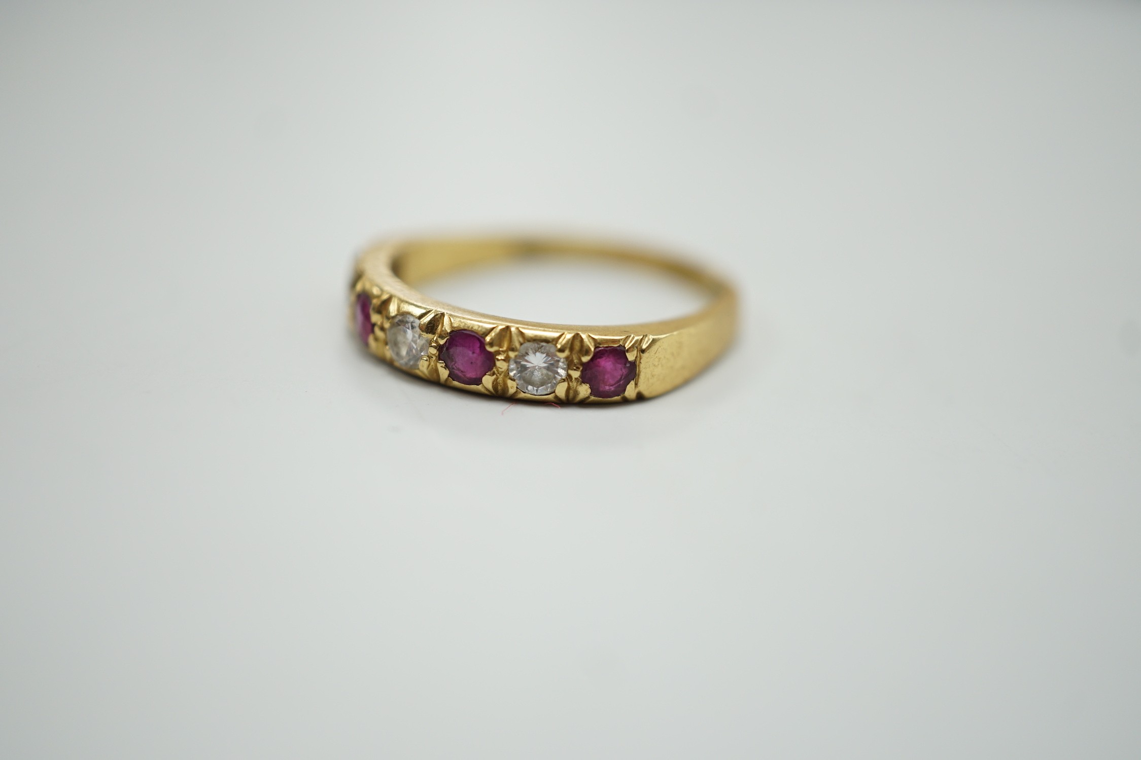 A modern 18ct gold, four stone ruby and three stone diamond set half hoop ring, size L/M